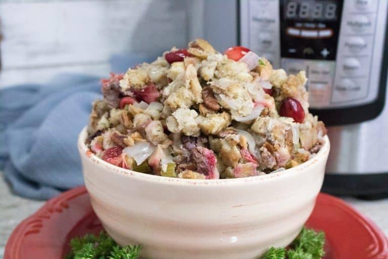 Finished Instant Pot Cranberry Pecan Stuffing in a white bowl set on a red serving plate in front of the Instant Pot