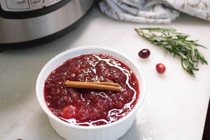 Instant Pot Cranberry Sauce in a white serving bowl and garnished with a cinnamon stick
