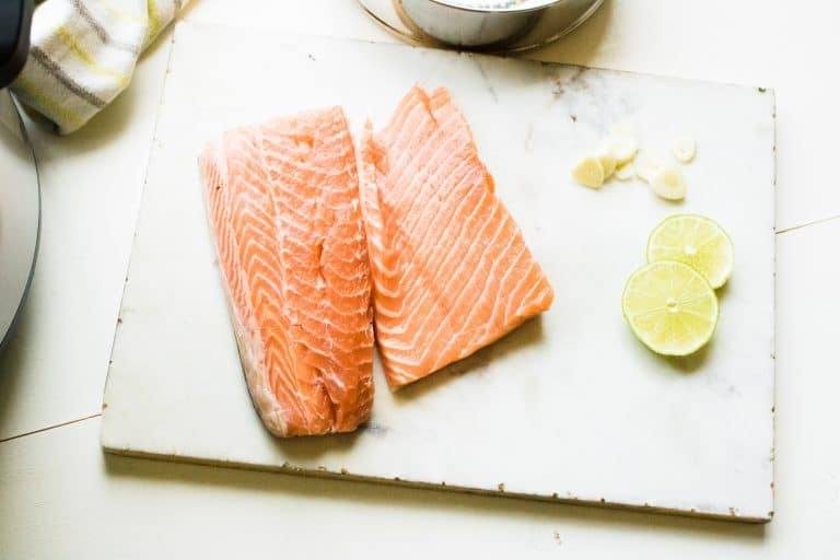 raw salmon for instant pot lemon garlic salmon sitting on cutting board with sliced lemons next to it