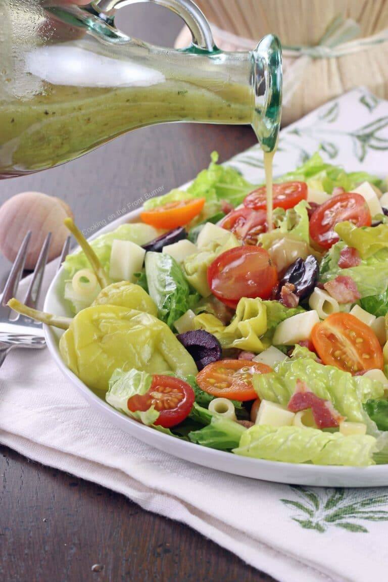 Homemade Italian dressing being poured over an Italian chopped salad with romaine, tomatoes, olives, pepperoncini and provolone