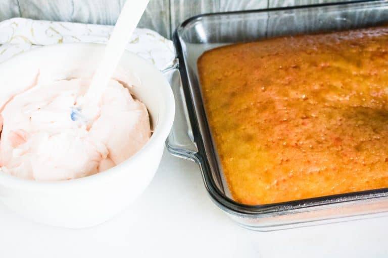 close up view of the poke cake next to a white mixing bowl containing the blended cream cheese mixture