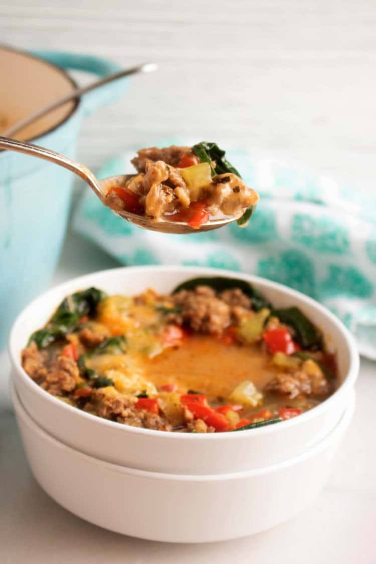 Spoonful of keto sausage and pepper soup lifted from a bowl topped with melted cheese