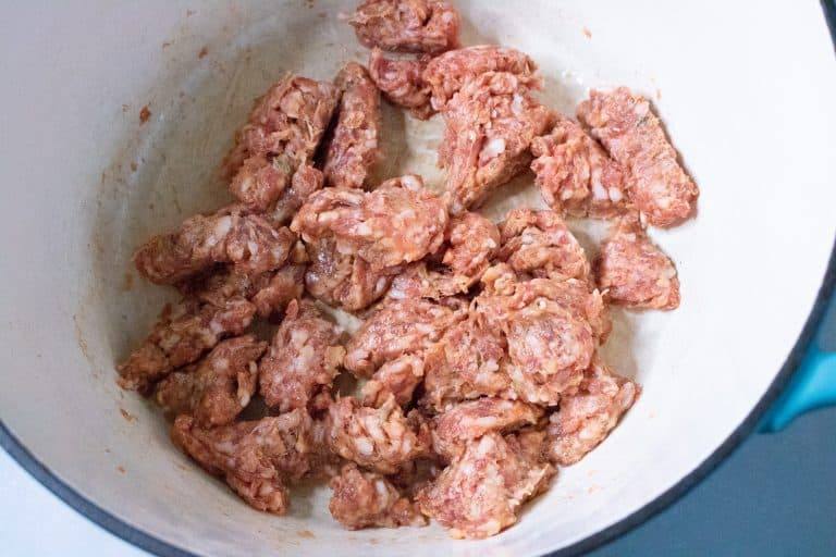 Crumbled raw Italian sausage starting to brown in a Dutch oven