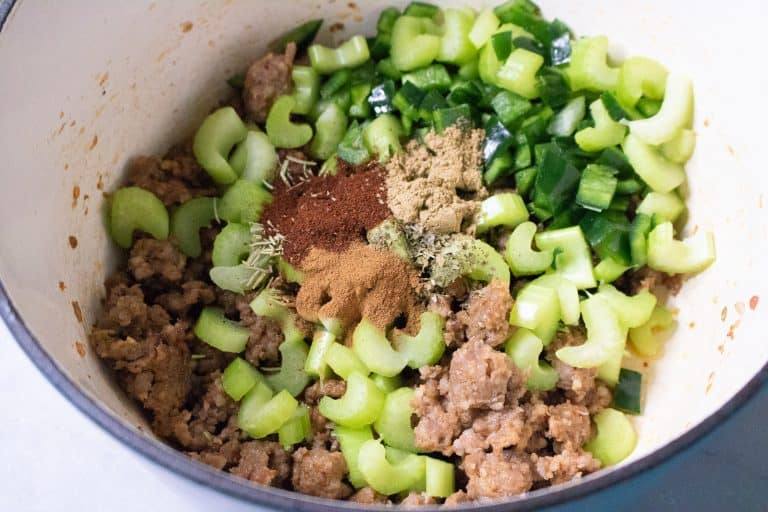 Browned sausage topped with celery, Poblano pepper, dried herbs and spices in a Dutch oven