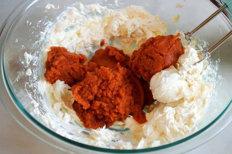 Pumpkin puree added to whipped cream cheese in a glass bowl for the pumpkin cream cheese filling