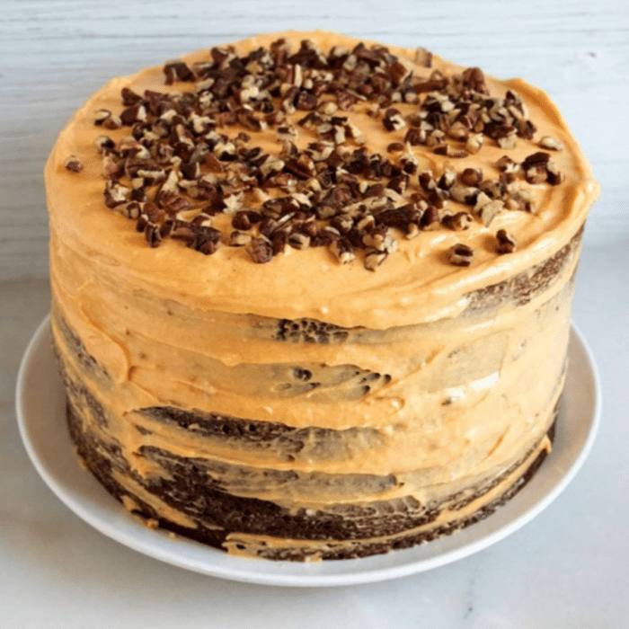 Layered chocolate cake with pumpkin cream cheese frosting topped with chopped pecans on a white plate