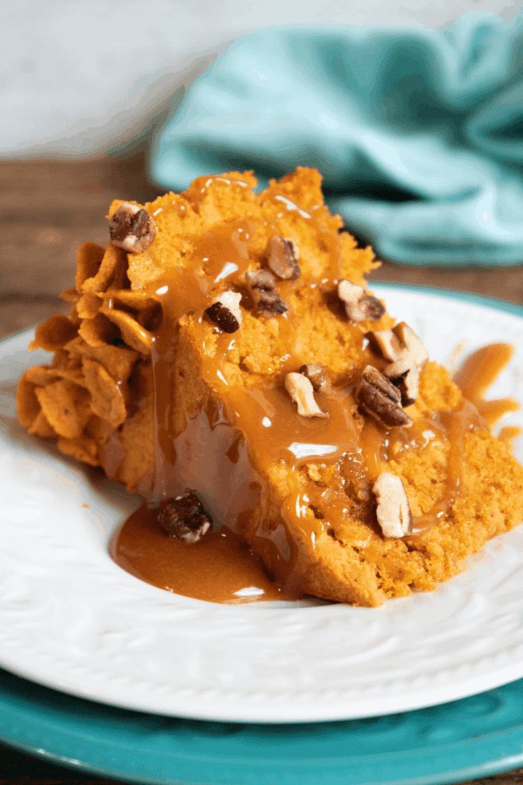 Slice of layered pumpkin cake with pumpkin ganache filling, caramel sauce, and pecans on a white plate