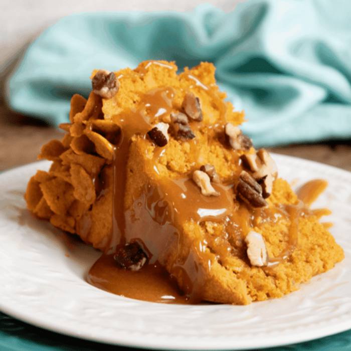 Slice of layered pumpkin cake with pumpkin ganache filling, caramel sauce, and pecans on a white plate