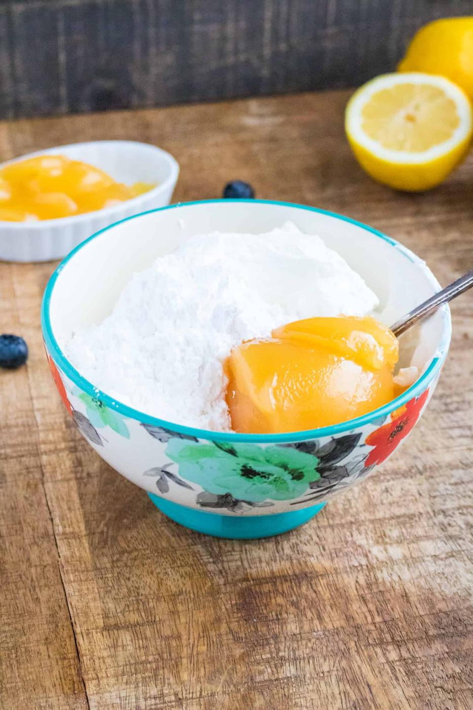 whipped cream and lemon curd in a small floral bowl with cut up lemons and a white bowl filled with lemon curd in the background