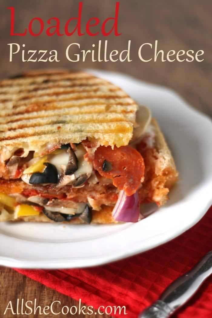 Loaded pizza grilled cheese sandwich cut open to show pepperoni, olives, mushrooms and melted cheese