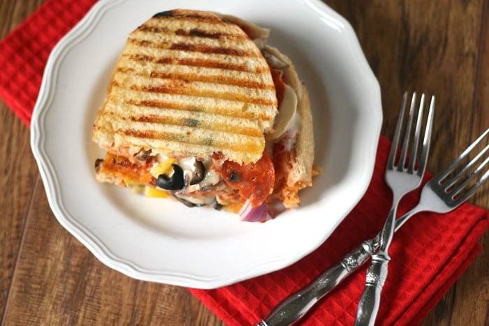 Overhead view of a loaded pizza grilled cheese on a white plate with forks and a red napkin