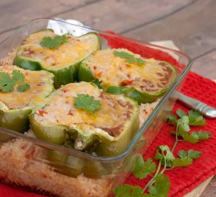 Mexican stuffed peppers topped with melted cheese and cilantro in a glass baking dish of Mexican rice