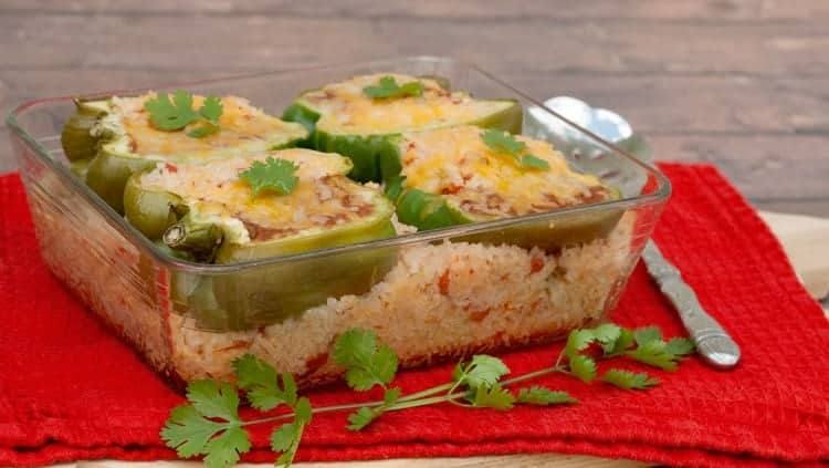 Stuffed peppers on a bed of Mexican rice in a glass dish on a red towel with cilantro