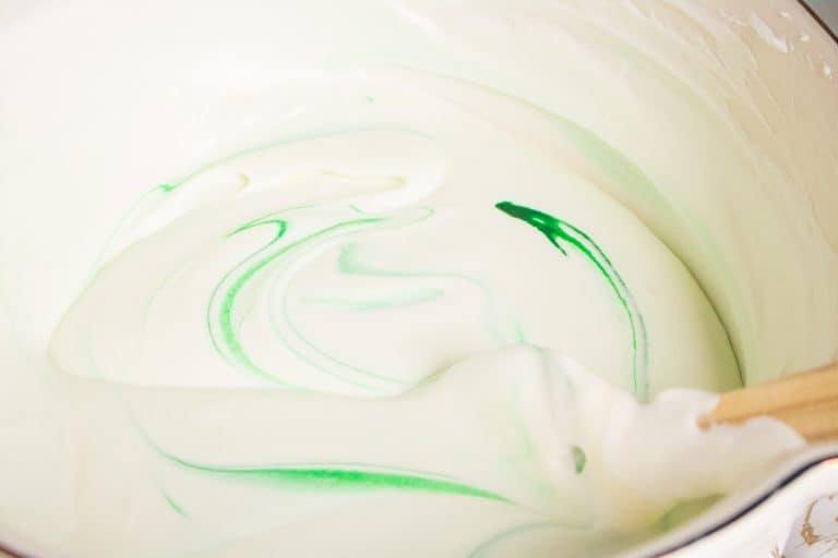 green food color being added to a bowl of mint chip no churn easy homemade ice cream mixture