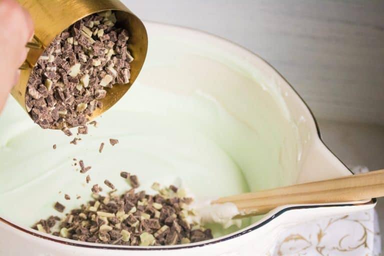 a scoop of mint chips being poured into a bowl of mint chip no churn easy homemade ice cream