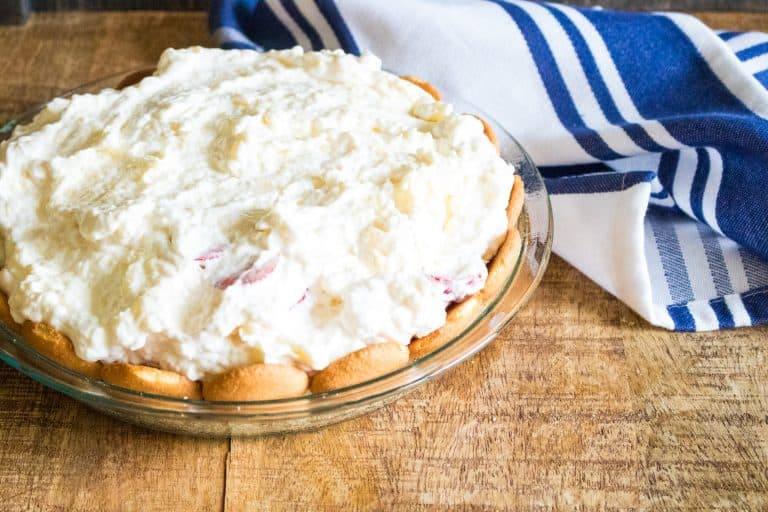 completed no bake tropical cream pie in pie plate on wooden table with blue and white striped towel in background