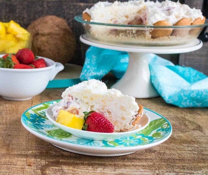 A slice of No-Bake Tropical Cream Pie served on a blue print plate set in front of a cake stand holding the rest of the pie