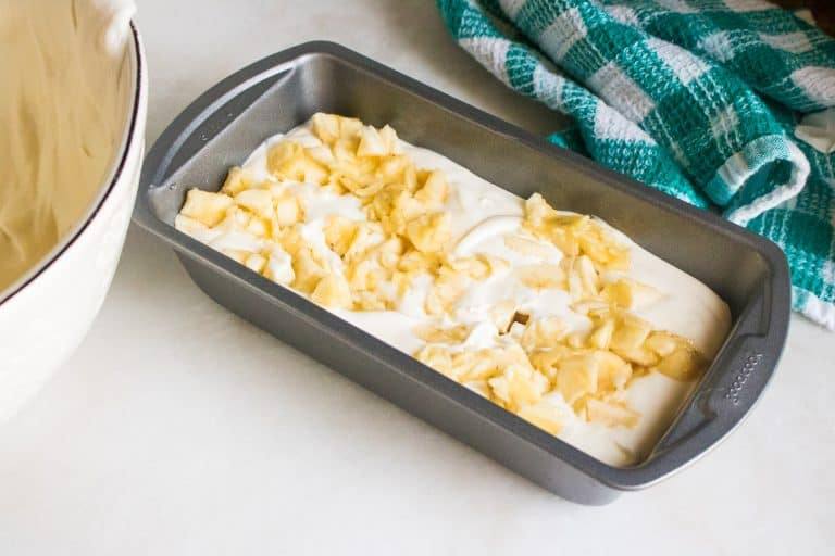 Bananas, chocolate chips and no-churn ice cream being played together in a bread pan to make No-churn banana chocolate chip ice cream