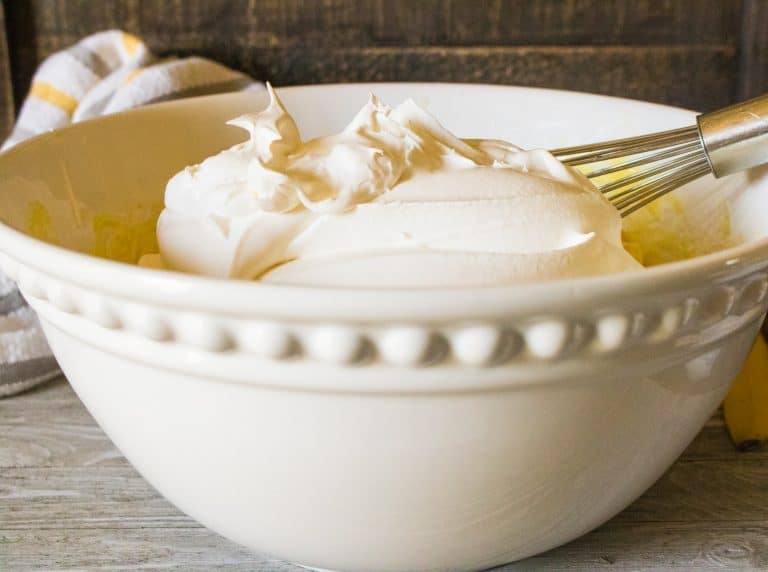 white ceramic bowl with whipped heavy cream for no-churn peanut butter ice cream in it with silver whisk
