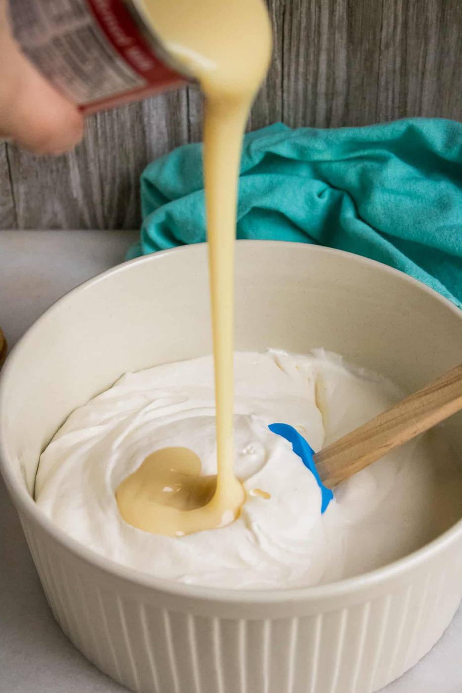 Whipped cream in bowl with can of sweetened condensed milk being poured into the bowl