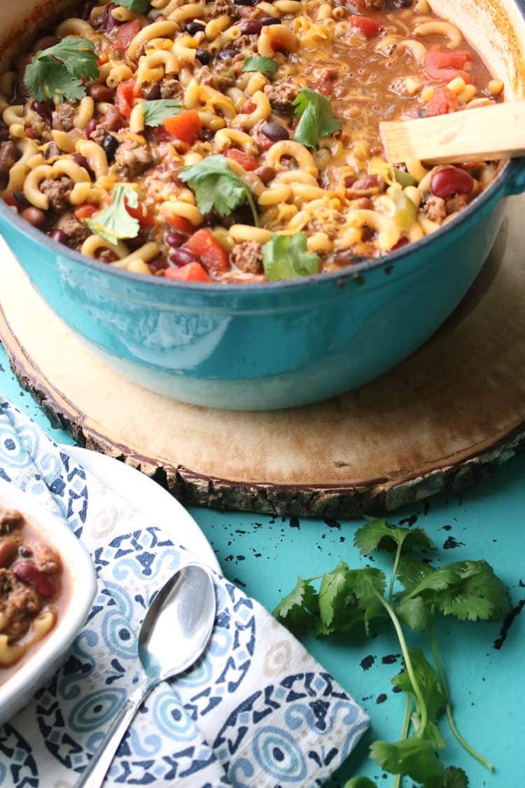 Chili mac and cheese in a large blue serving pot with a bowl on the side