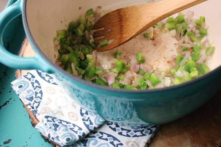Sautéing onions and bell peppers in a blue pot