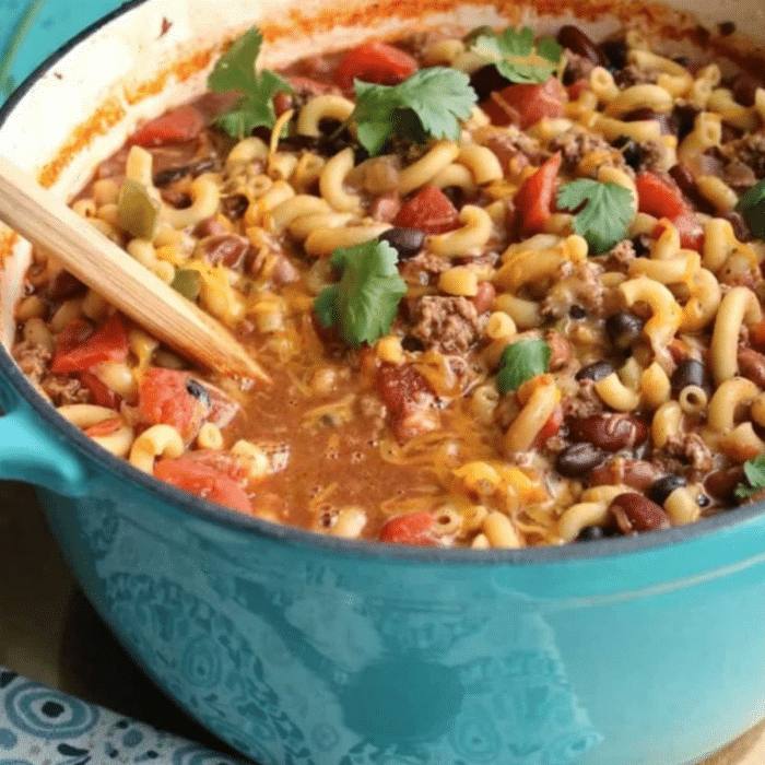 One-pot chili mac and cheese with beans, ground beef, and cilantro in a blue Dutch oven
