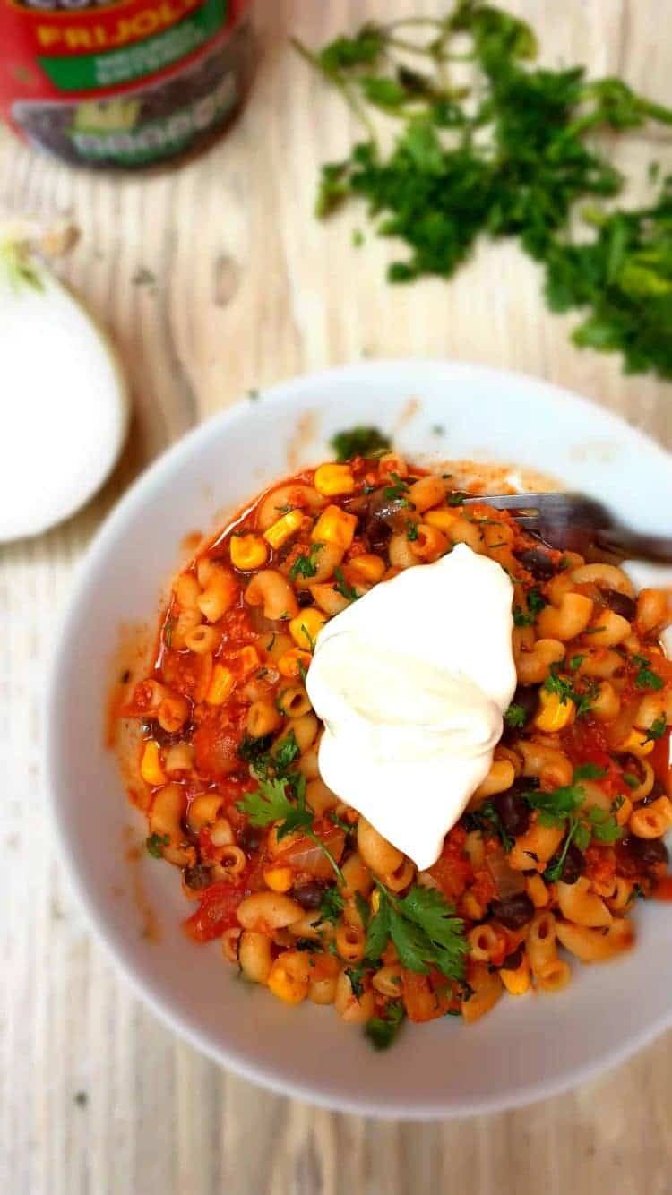 One-pot southwest chili mac in a white bowl with sour cream, cilantro and a fork