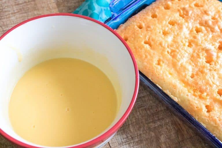 White cake baked with holes poked. Gelatin in bowl beside.