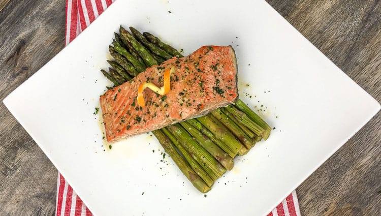 salmon plated over asparagus on white square plate