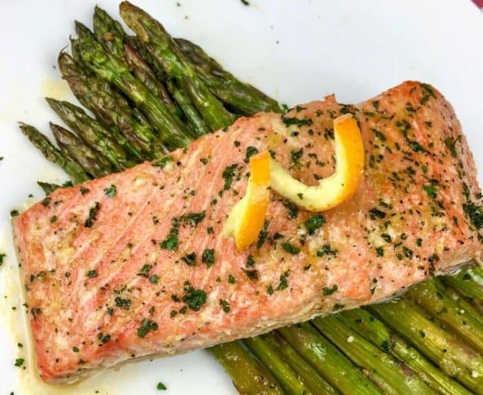 salmon plated over asparagus on white square plate