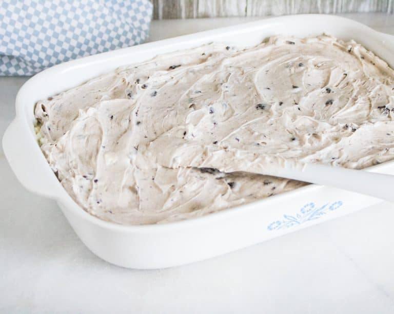 13x9 white corning ware pan with cake for oreo poke cake spread with oreo cream cheese topping and blue and white towel in background