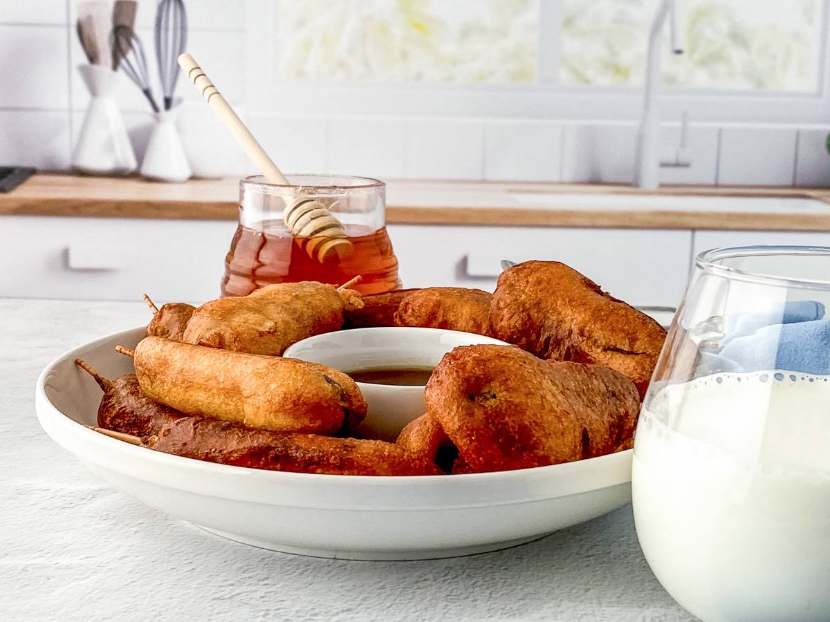 pancakes and sausages on sticks, being served on a serving tray