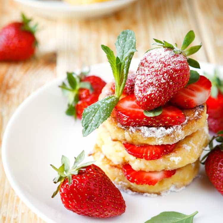 strawberry cheesecake pancakes being served wth strawberries on a white plate