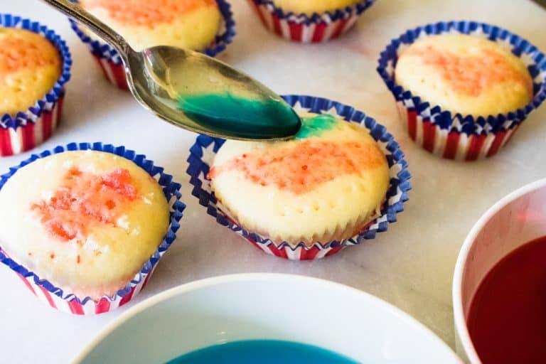 top-down view of blue gelatin being poured onto the top of poke cupcakes