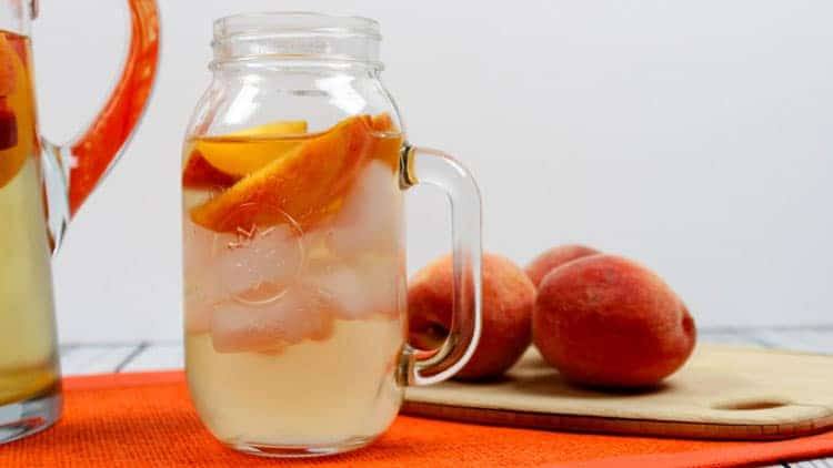 white wine and peach sangria in a mason jar and peaches on a cutting board