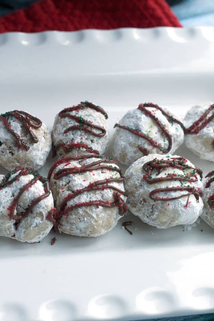 Close-up of peppermint snowball cookies dusted in powdered sugar with a chocolate drizzle