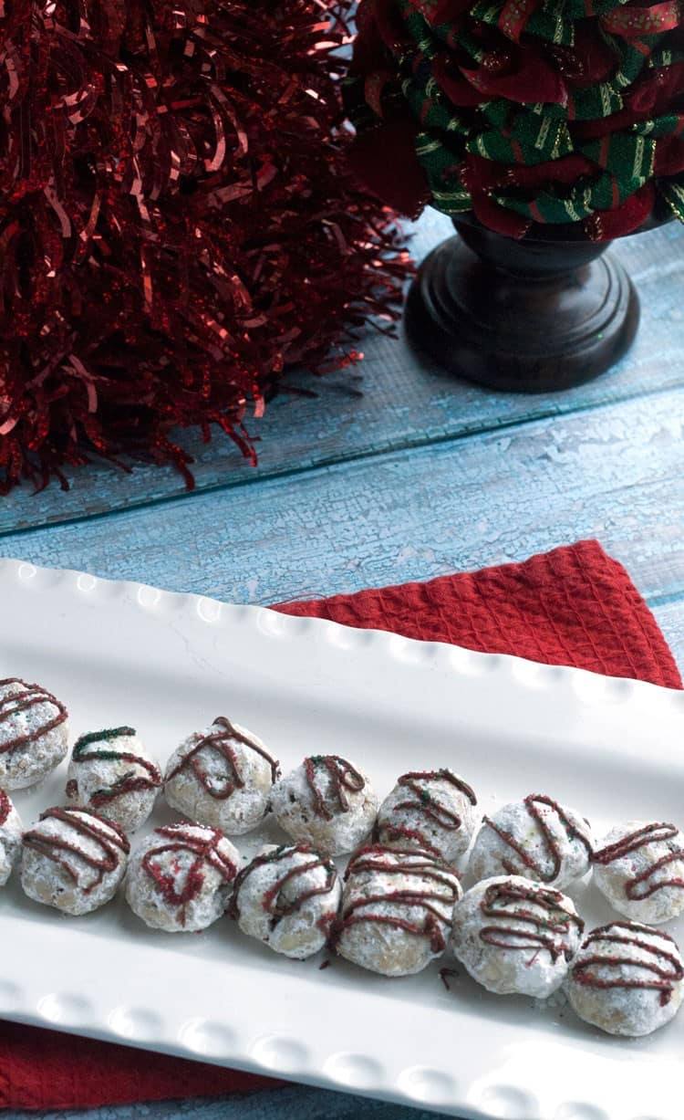 Peppermint snowball cookies drizzled with chocolate on a white platter with red holiday tinsel
