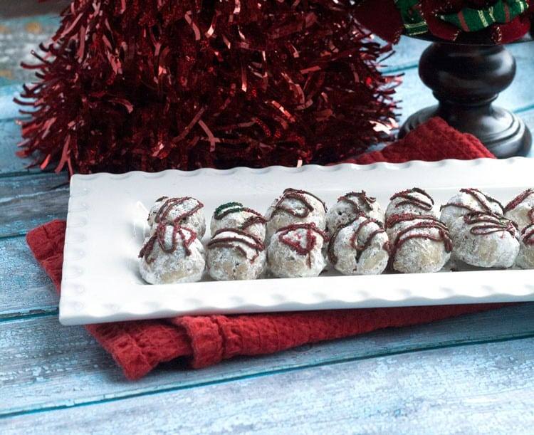 A platter of peppermint snowball Christmas cookies with red tinsel and a red napkin