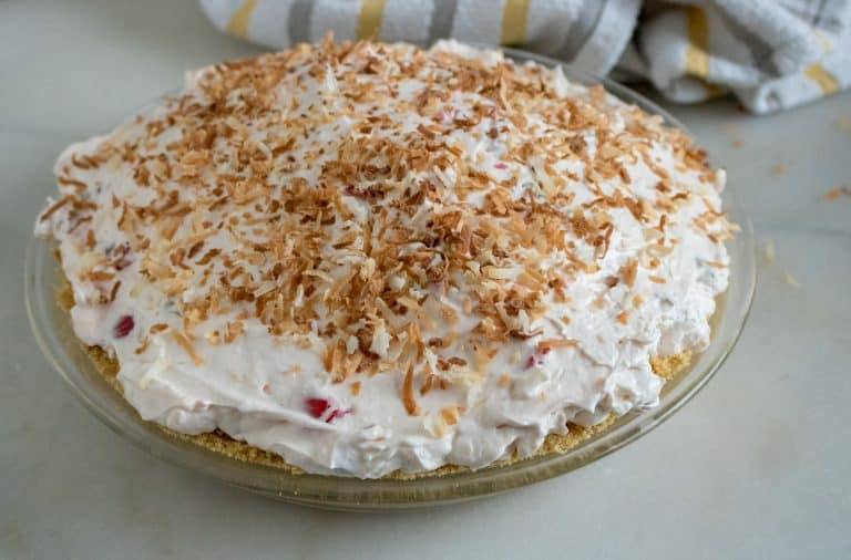 Assembled pie in a pie plate. Graham cracker crust, cream cheese mixture and whipped topping with toasted coconut garnish