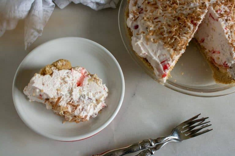 Once slice of Piña Colada Pie served on a white plate with whole pie beside and two forks
