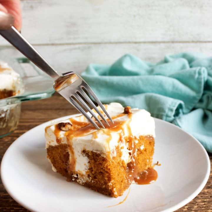 Fork cutting into a slice of pumpkin poke cake topped with caramel and pecans