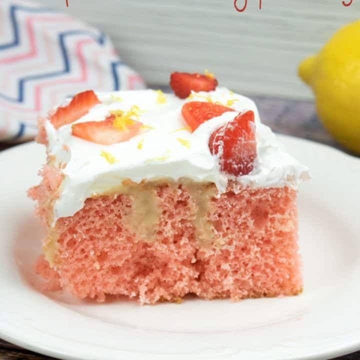 strawberry poke cake with slices strawberries on top, on a white plate with a lemon and colorfully striped napkin in the background
