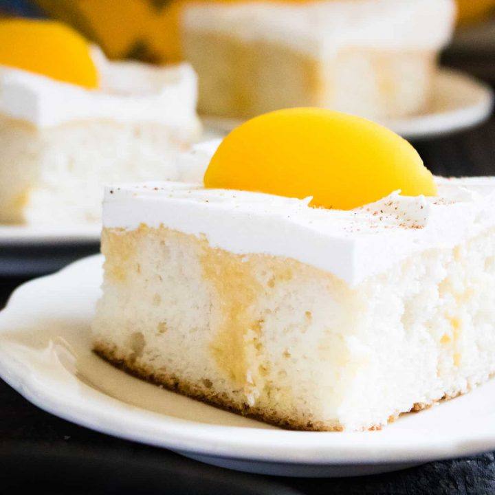 Two slices of Summer Peach Poke Cake served on white dessert plates