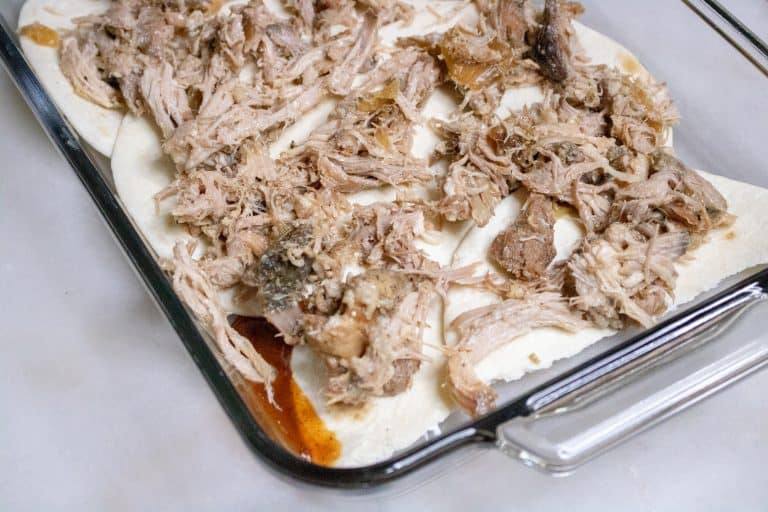 Shredded pork for pork enchilada casserole spread on top of flour tortillas.