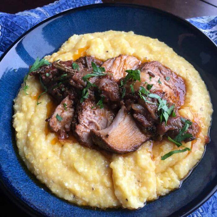 sliced roasted pork butt on creamy polenta on a blue plate
