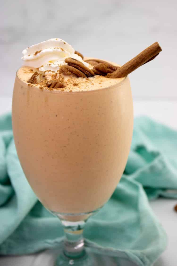 Close-up of a pumpkin cheesecake milkshake topped with whipped cream, pecans and a cinnamon stick