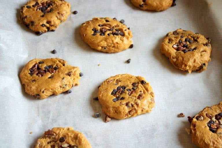Flattened rounds of pumpkin chocolate chip cookie dough lined up on a parchment-lined baking sheet