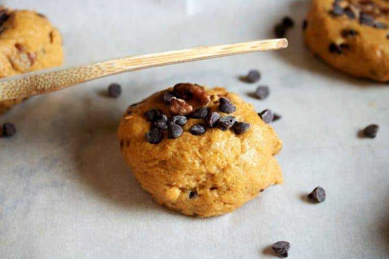 A ball of pumpkin chocolate chip cookie dough topped with pecans and mini chocolate chips on parchment paper