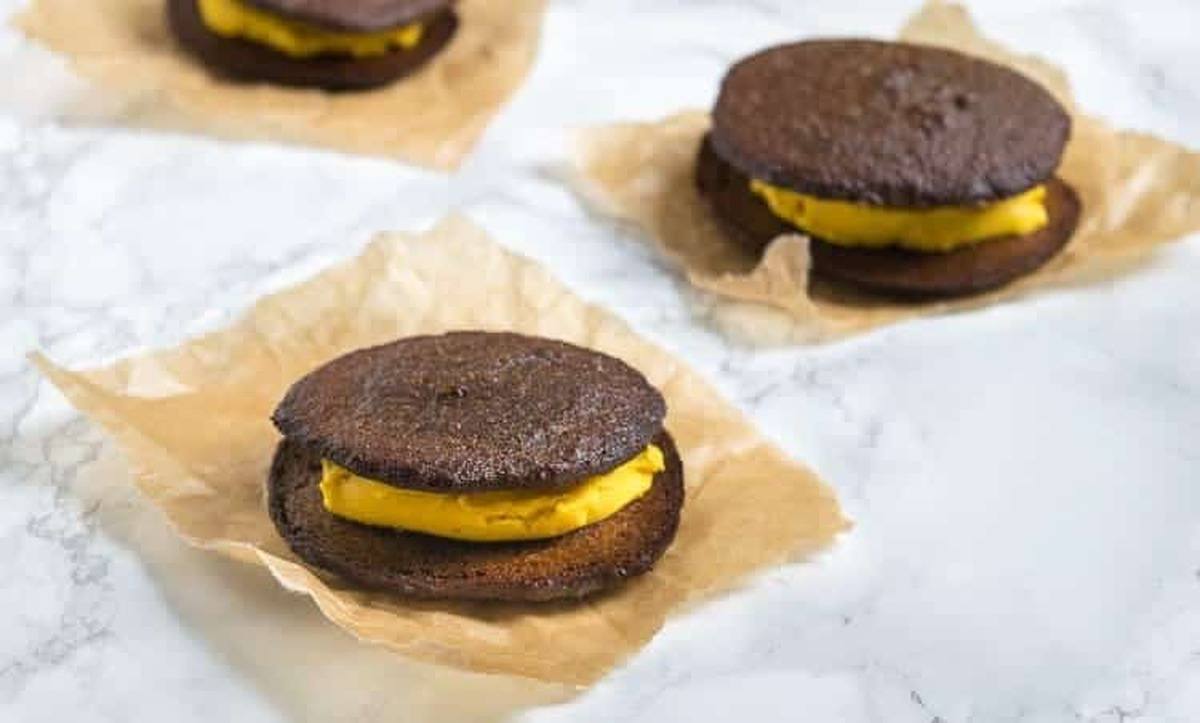 Pumpkin whoopie pies filled with pumpkin cream on squares of parchment paper on a marble counter